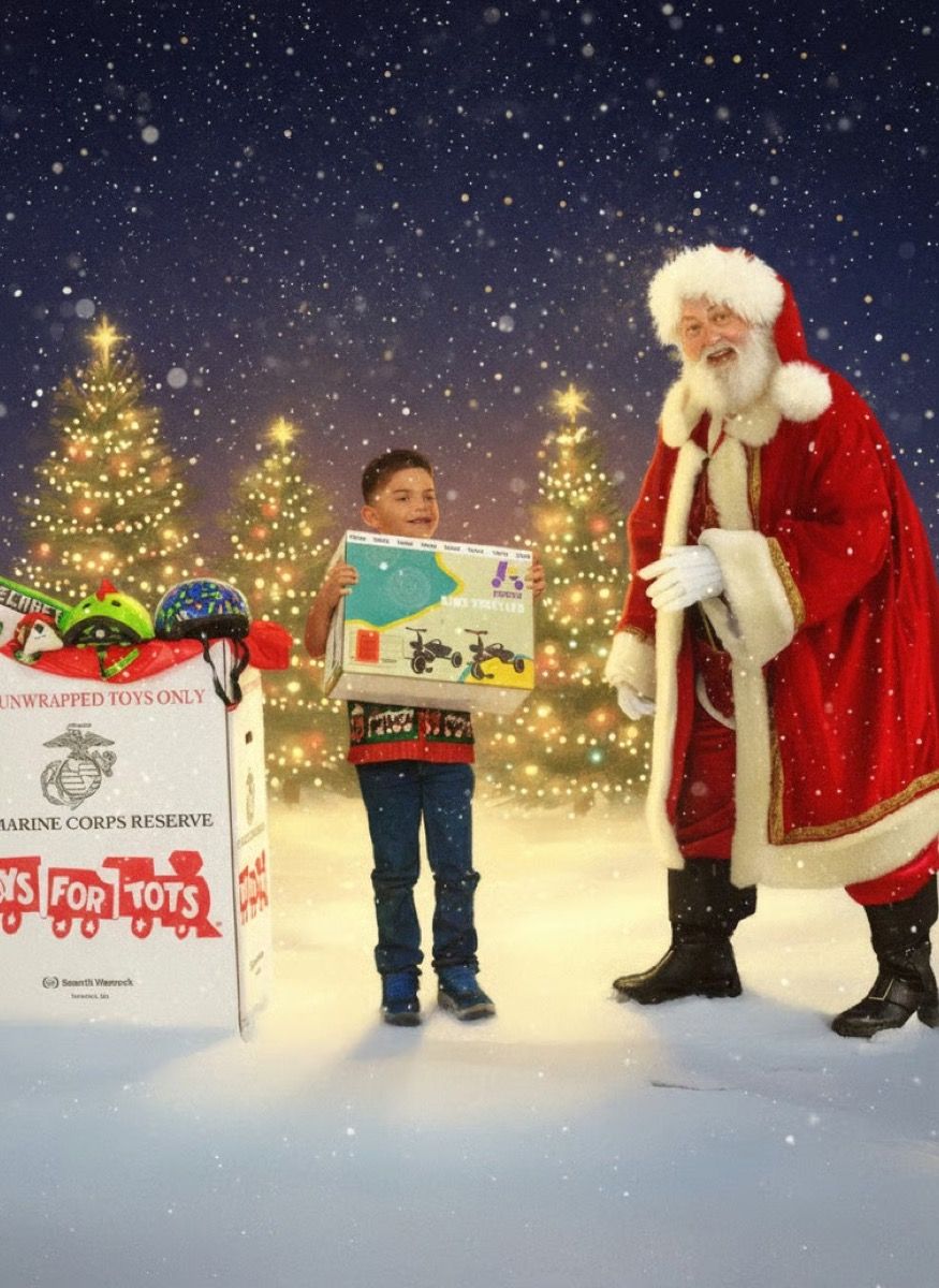 Santa Glenn with a boy holding a picture book beside a Toys for Tots donation box