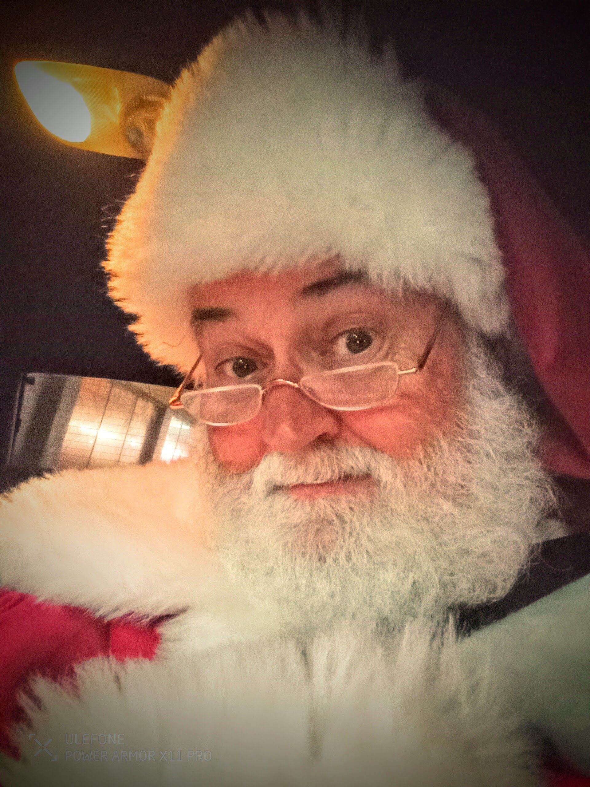 Close-up of Santa Glenn smiling over his glasses by lantern light
