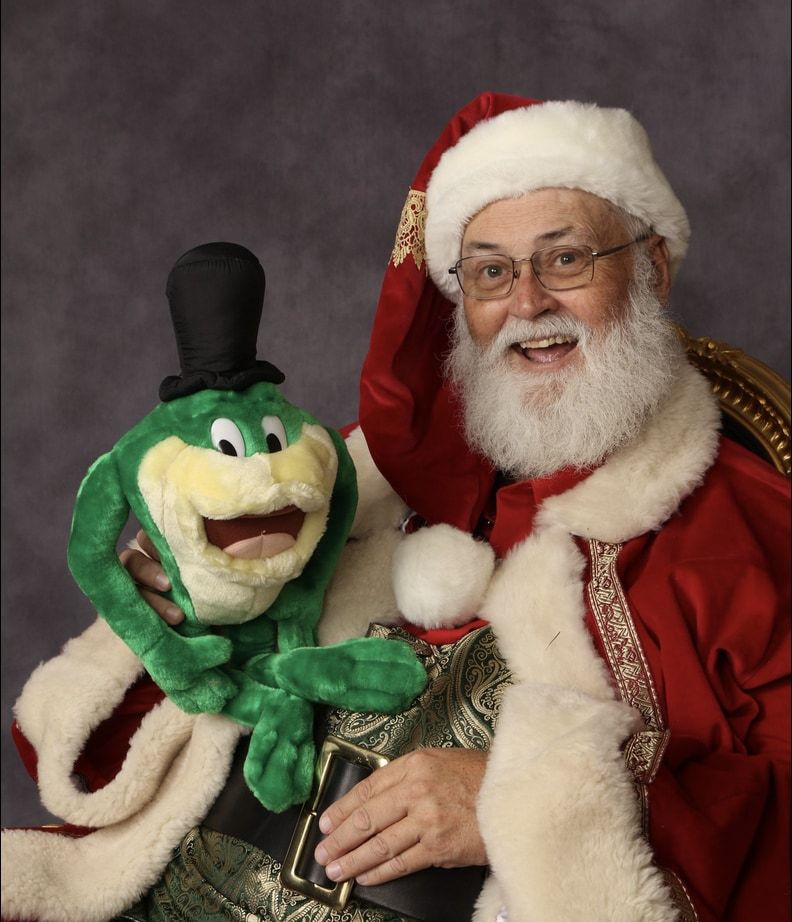 Santa Glenn laughing with a green frog puppet in a top hat