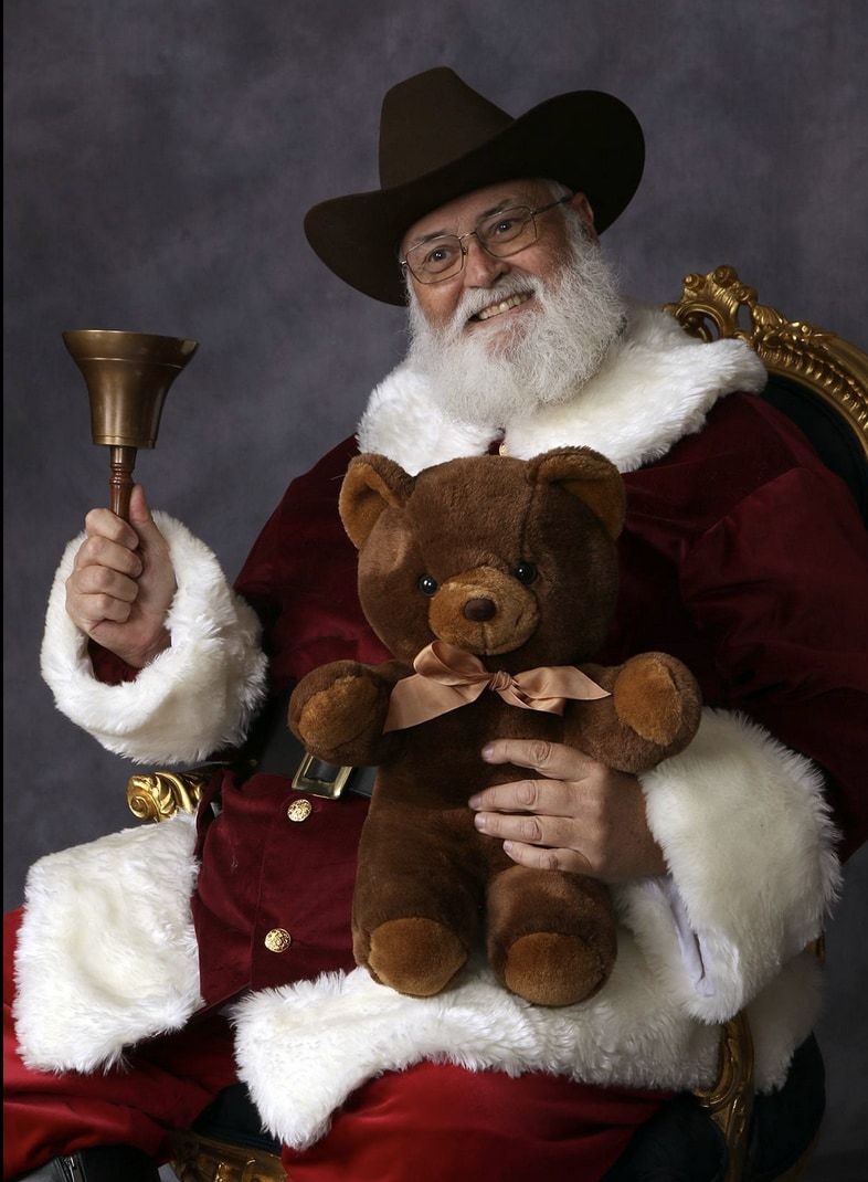 Santa Glenn in a brown cowboy hat, ringing a bell and holding a teddy bear