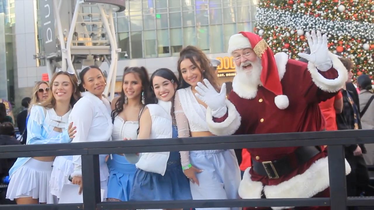Santa Glenn waving on stage with a group of young women at a tree lighting