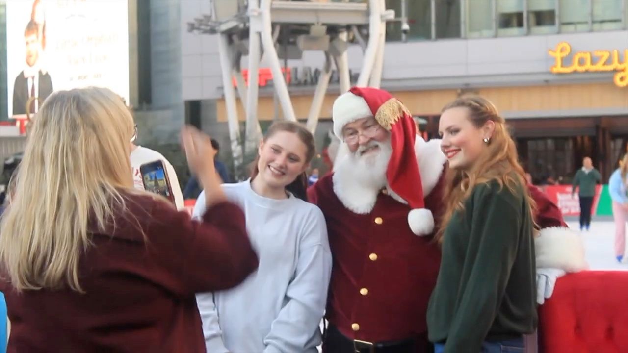 Santa Glenn posing with two smiling teenage girls while a friend takes their photo