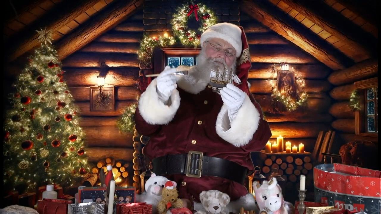 Santa Glenn in a log cabin surrounded by toys, candles and a lit tree