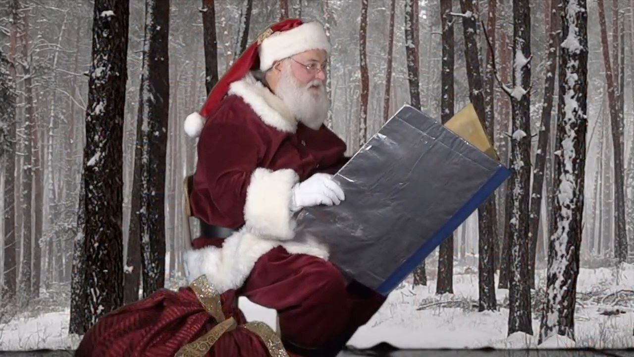 Santa Glenn reading a large storybook in a snowy forest